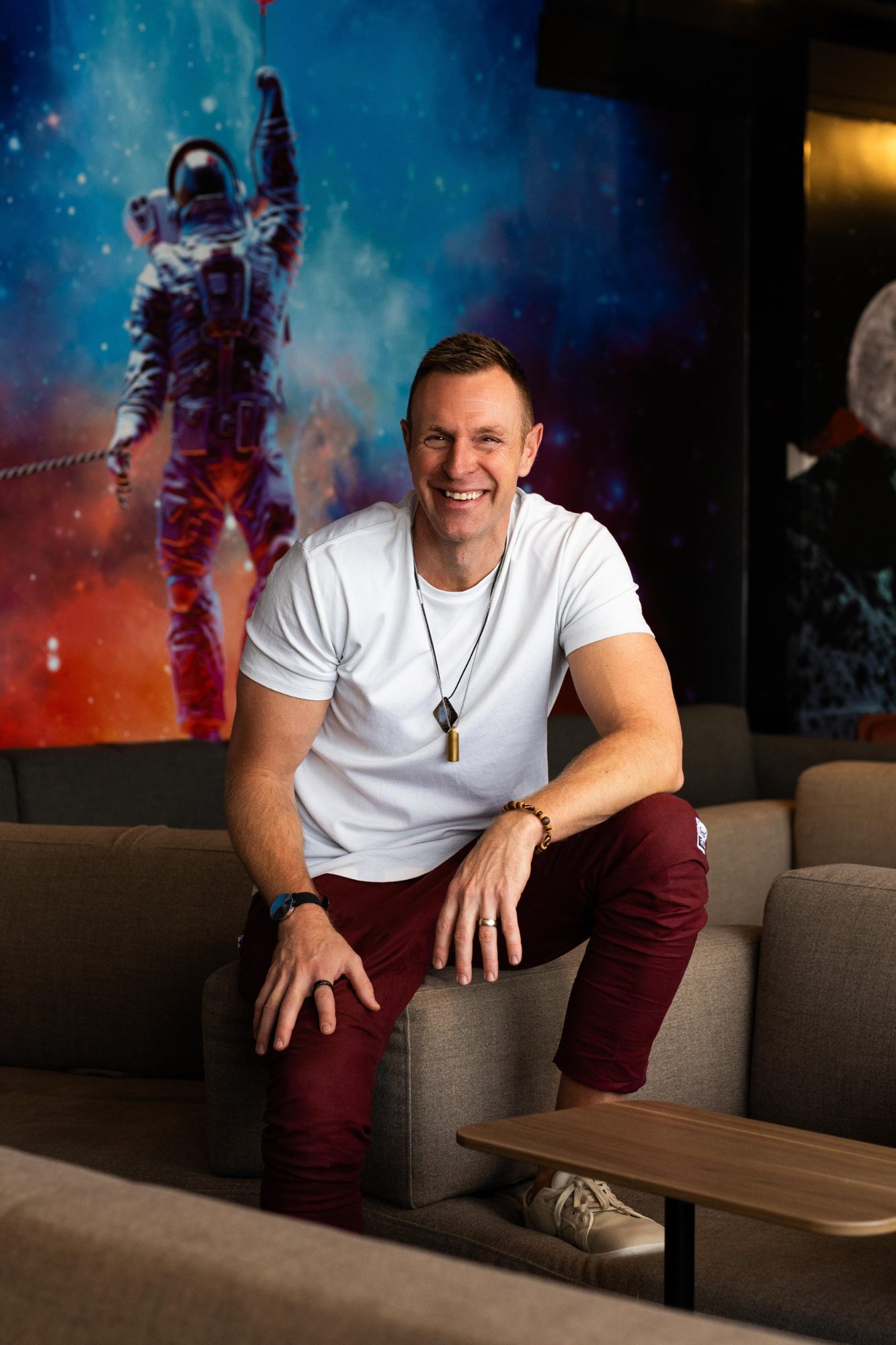 Darren Langille smiling, seated on a couch in front of a colourful astronaut mural